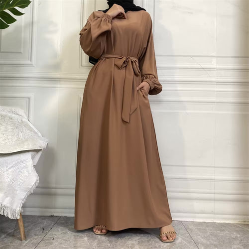 Brown dress with a belt worn by a woman in a minimalistic room.