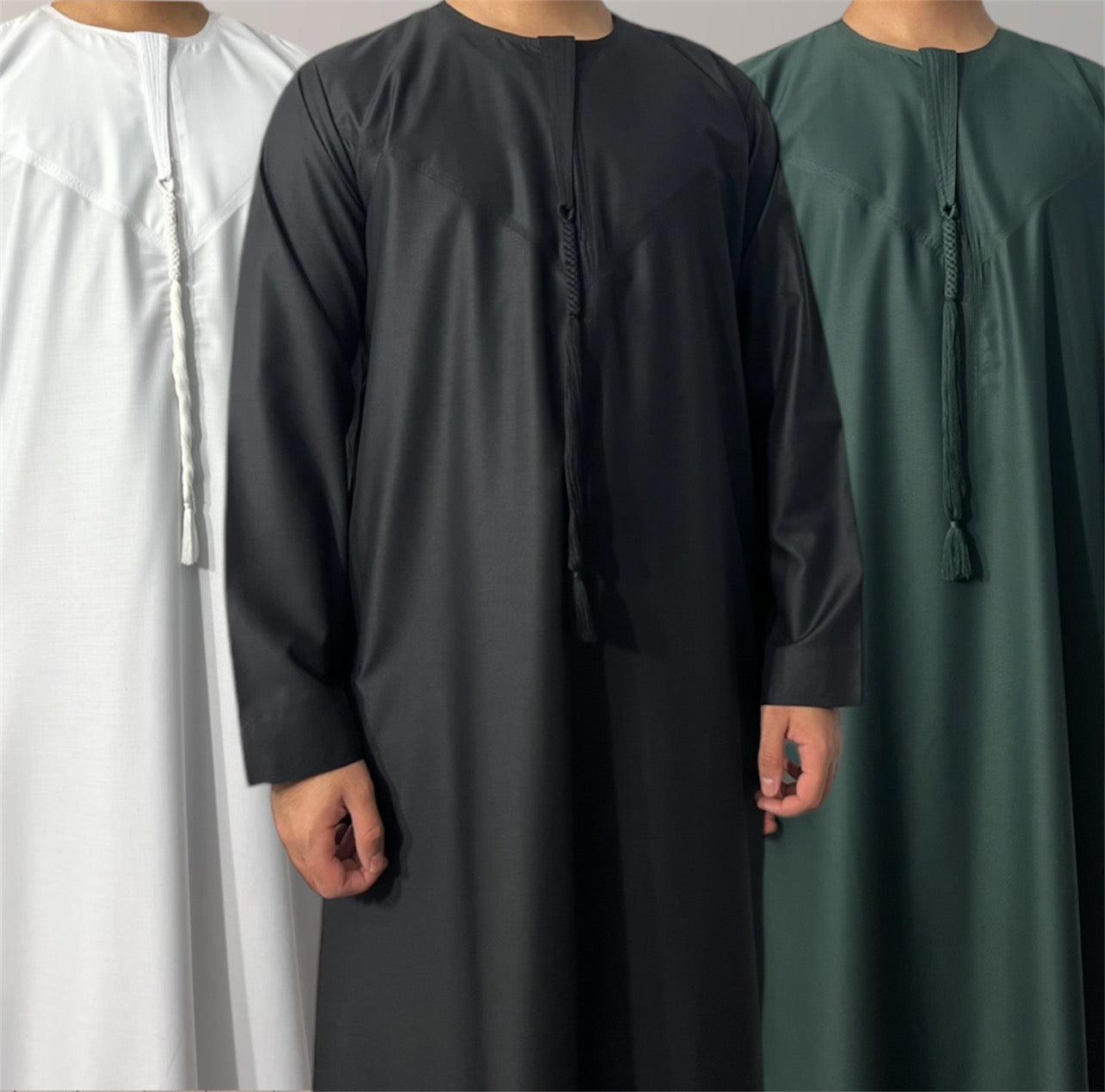 Three children wearing traditional Emirati thobes in white, black, and green colors.