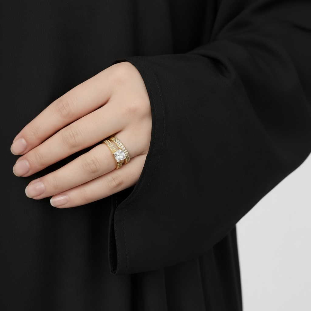Hand wearing a gold ring with a black sleeve on a neutral background