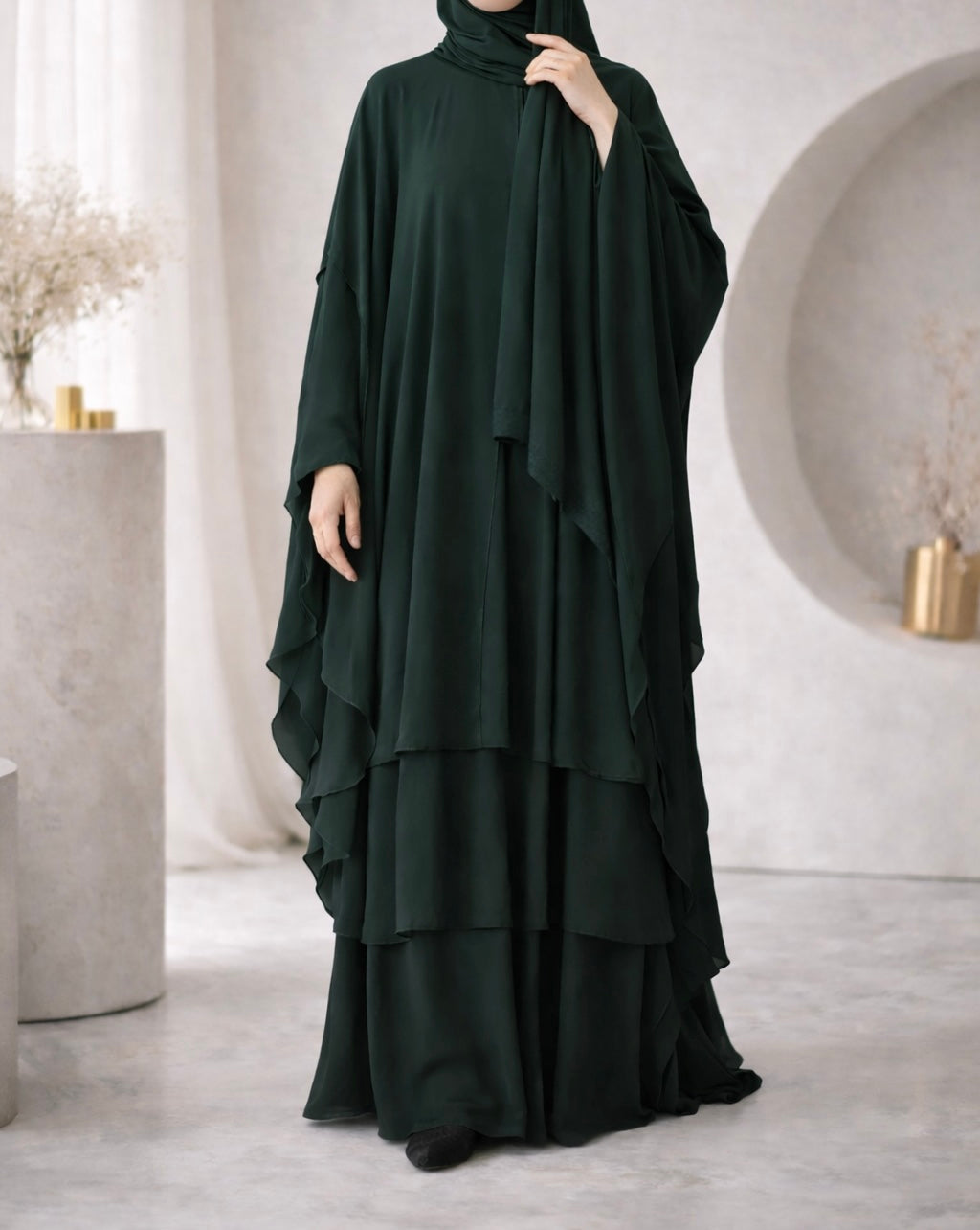 Dark green abaya worn by a model in a minimalistic room with white walls and light-colored floor.