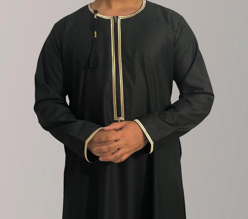 A child model wearing a black Omani thobe with gold accents.