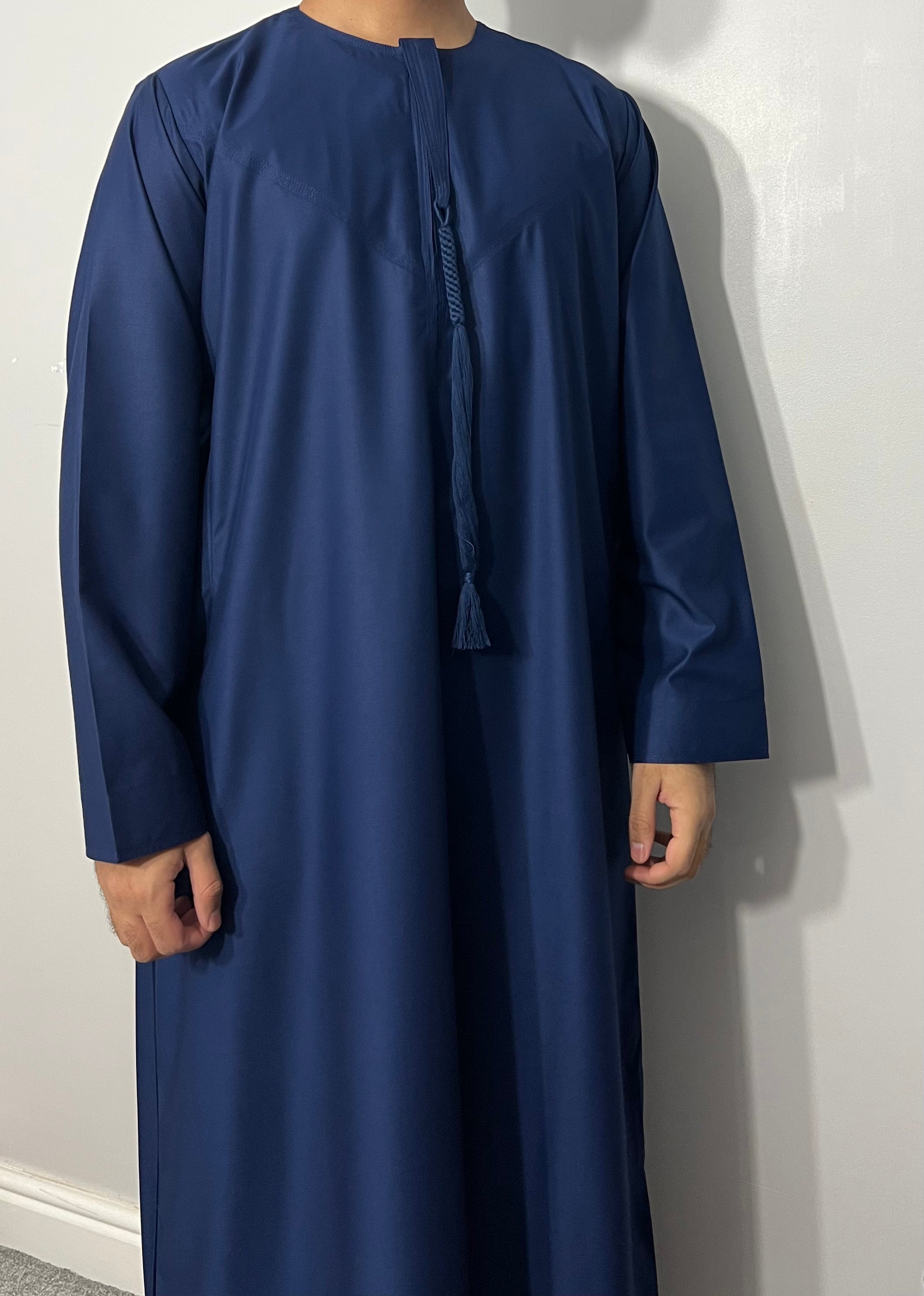 A man wearing a navy blue Emirati thobe with a chest zip opening and side pockets, featuring a traditional Emirati tassel.