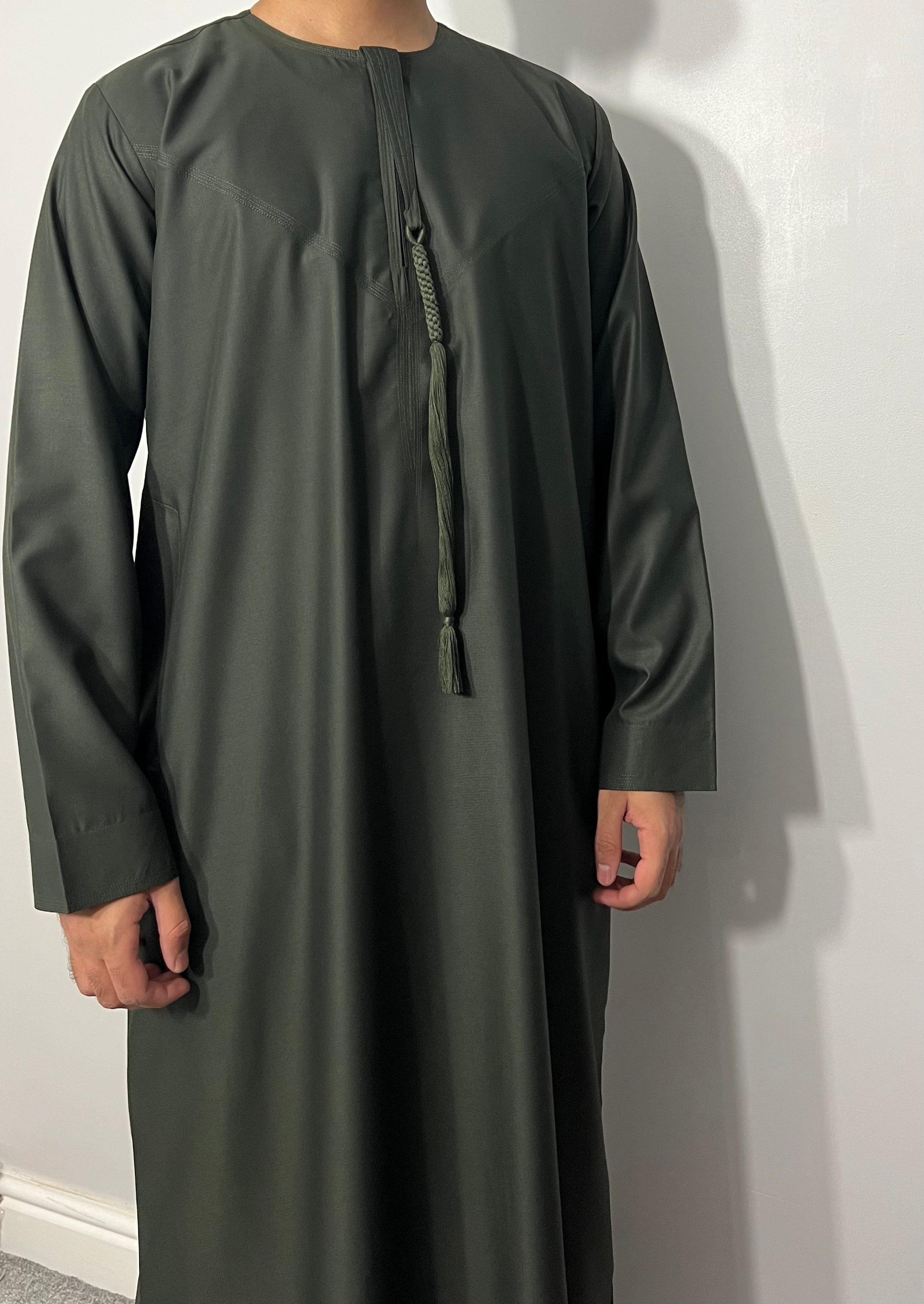 A man wearing a green traditional Emirati thobe with a chest zip opening and Omani tassel.