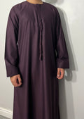 A man wearing a maroon traditional Emirati thobe with a chest zip opening and side pockets.