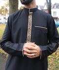 Man wearing a blackcollard thobe outfit with gold embroidery in an outdoor setting