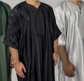 Two men wearing moroccan thobe outfits, one in black and the other in white, against a neutral background.